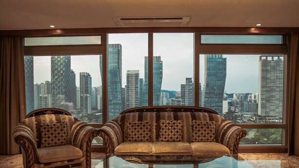 A room with a large window offering a cityscape view, a sofa, and two armchairs.