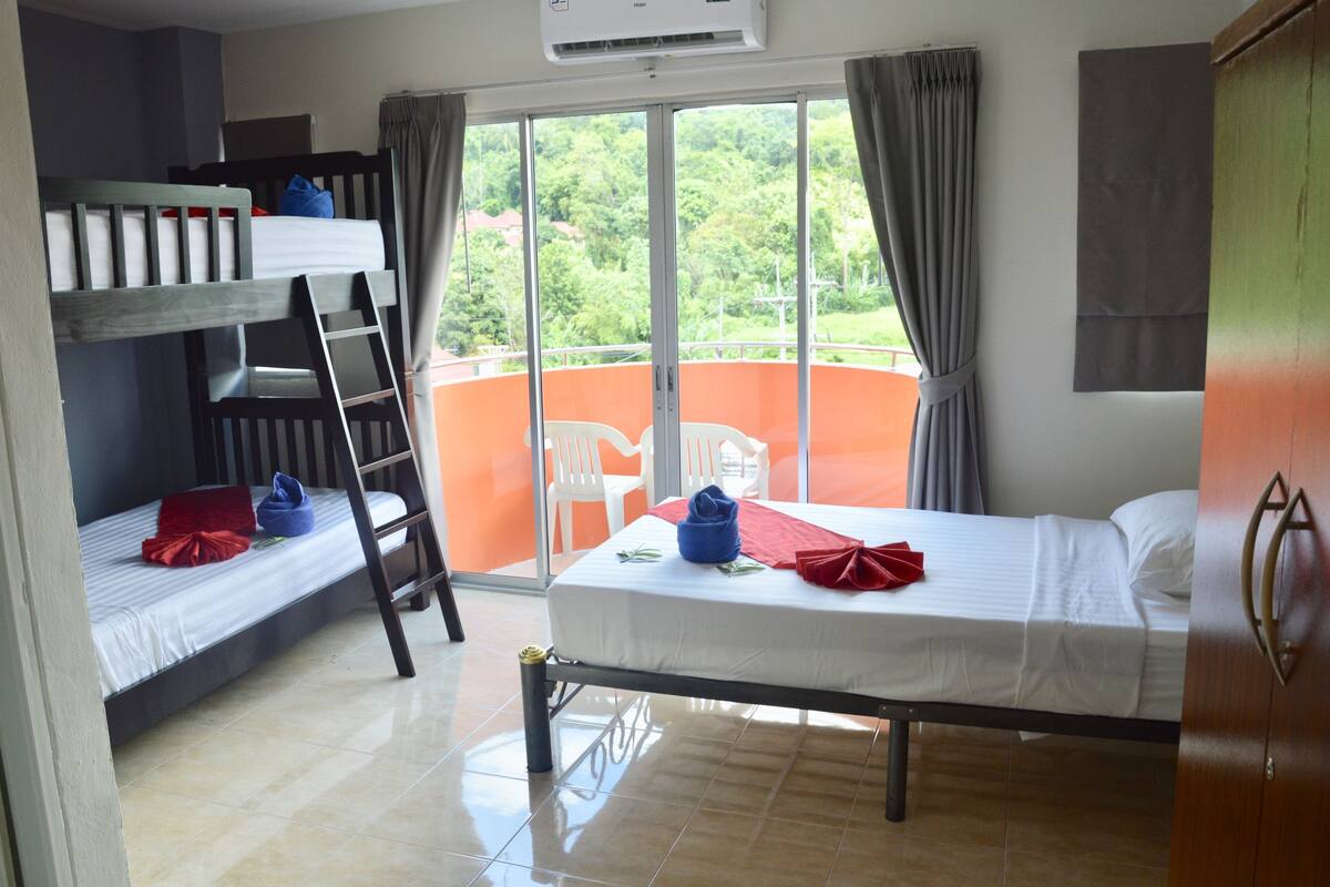 A room with two bunk beds, a balcony with a view, and a wooden wardrobe.