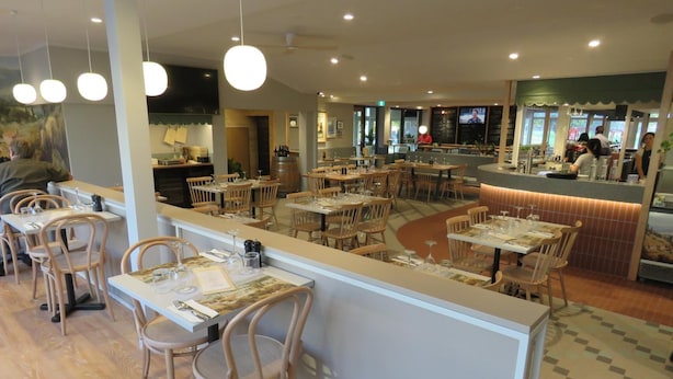 A restaurant with wooden tables and chairs, a counter with a menu, and a television screen in the background.