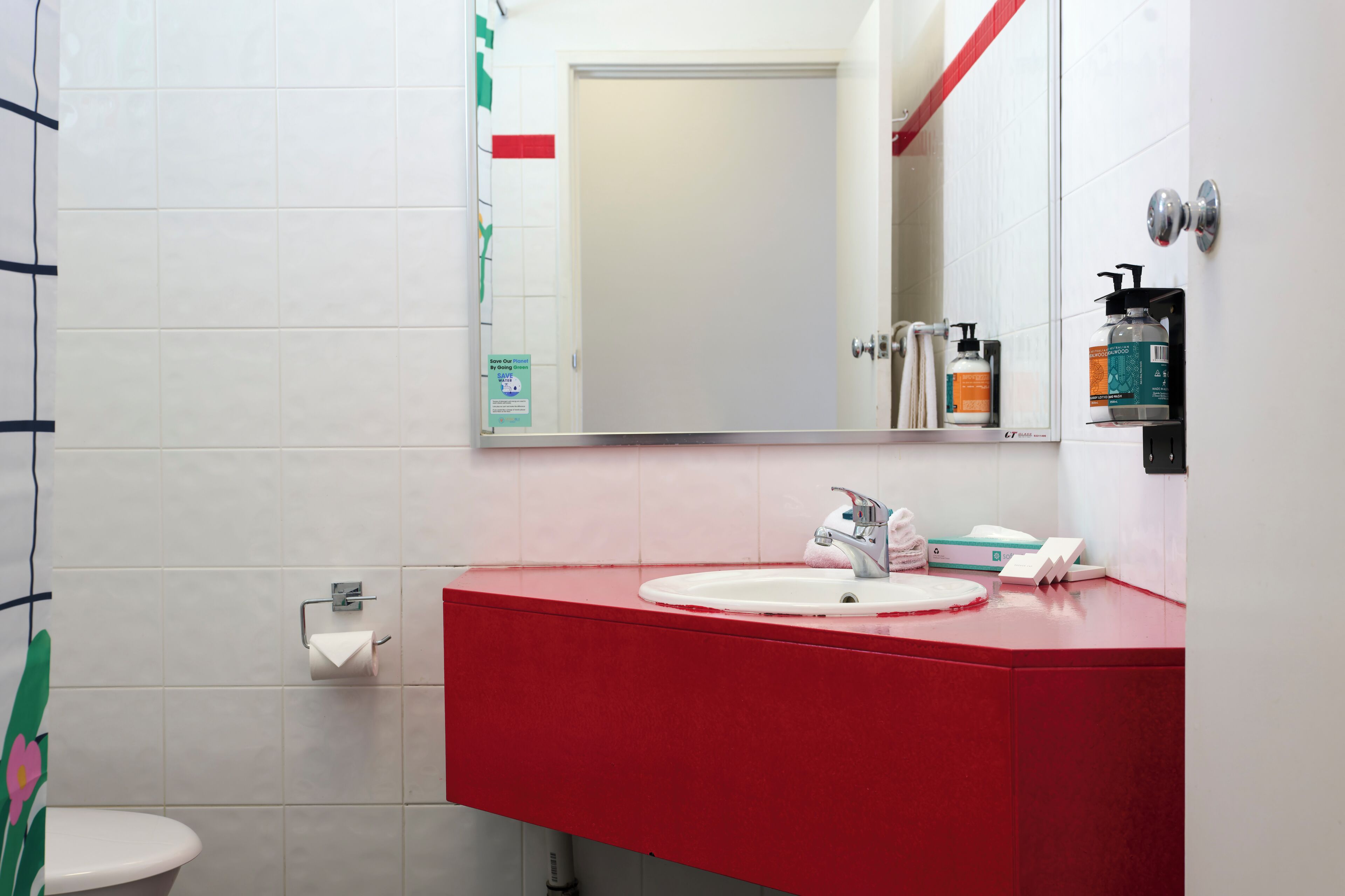 A bathroom with a red sink, white toilet, and a mirror.