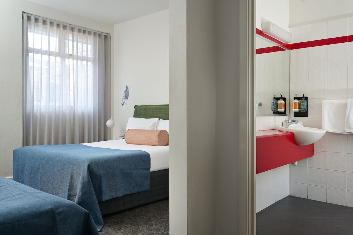 Camera d'albergo con due letti, bagno con un piano di lavoro rosso e finestra con tende.