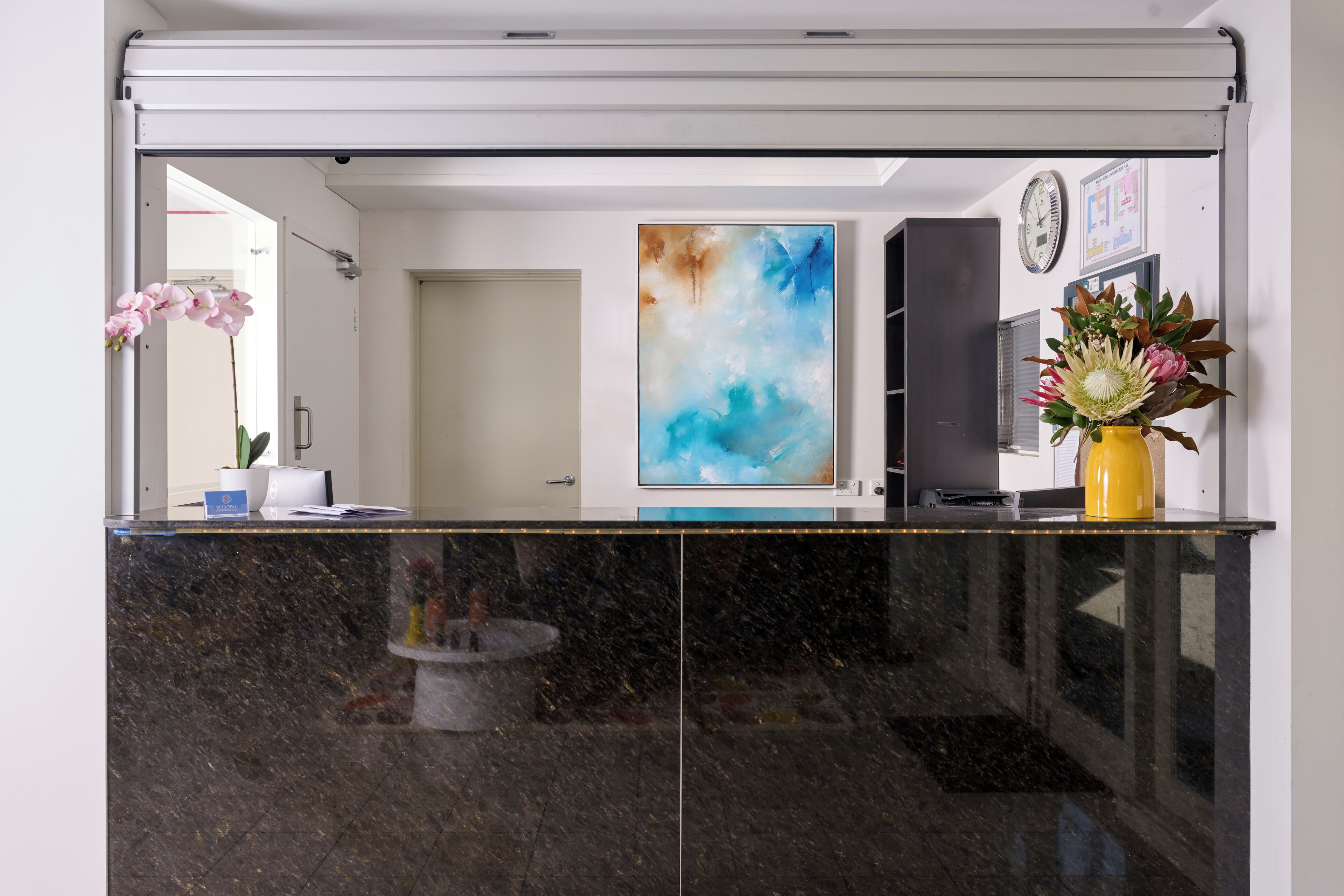 Un comptoir d’accueil avec un plateau en marbre, un tableau accroché au mur et un vase rempli de fleurs.