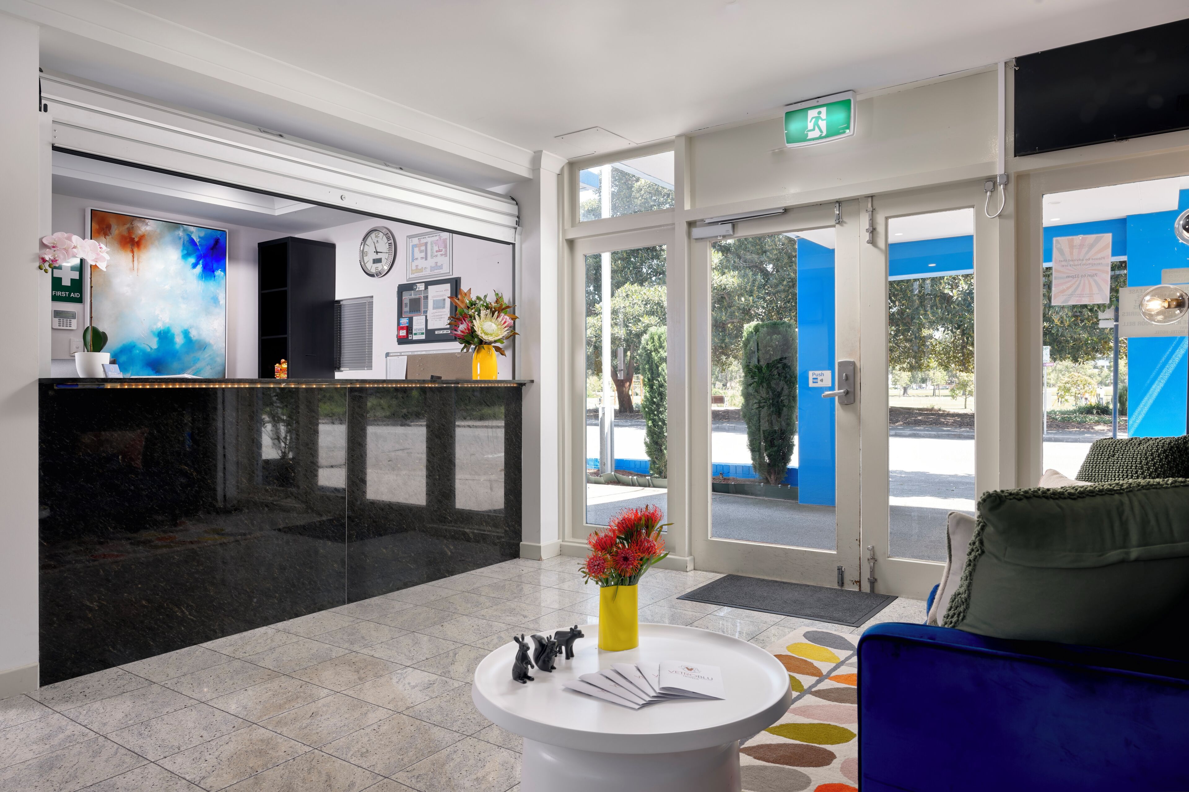 A reception area with a black reception desk, a clock, a first aid sign, and a flower vase.