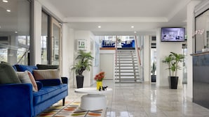 A modern hotel lobby with a blue sofa, a white coffee table, and potted plants.