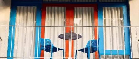 Un edificio con facciata blu e rossa, diverse finestre con tende e un balcone con sedie.