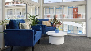 A room with two blue armchairs, a white coffee table, and a view of a balcony with a railing and a building in the background.