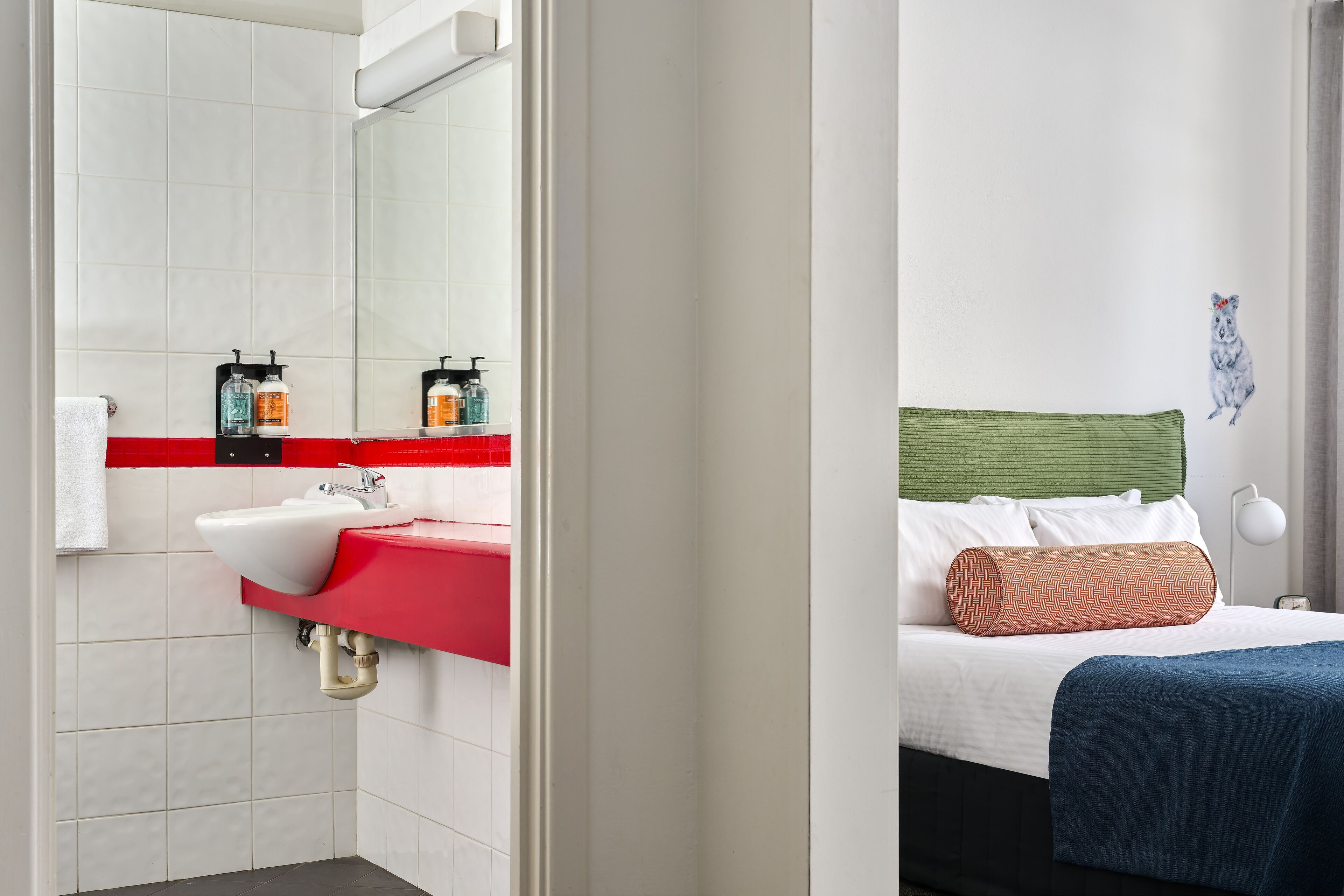 Ein modernes Badezimmer mit einem weißen Waschbecken, einer roten Arbeitsplatte und einem Spiegel.