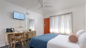 A hotel room with a bed, a desk with a chair, a television, and a ceiling fan.