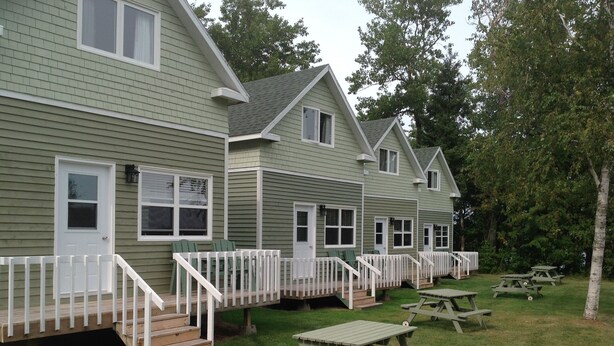 A row of green-roofed cabins with white railings and a grassy lawn with picnic tables. - Briarwood Coastal Cottages & Lodge (Union)