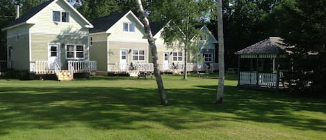A row of two-story houses with a front porch and a gazebo in a grassy yard.