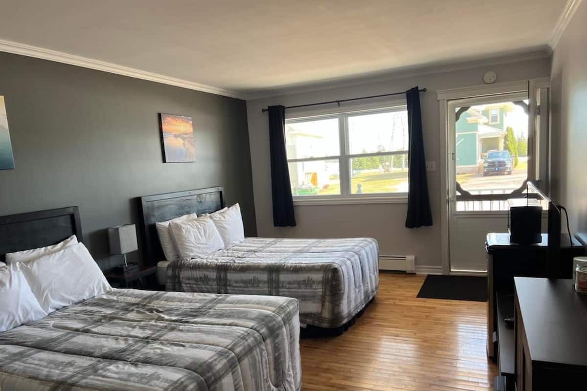 A hotel room with two beds, a desk, and a window with curtains.