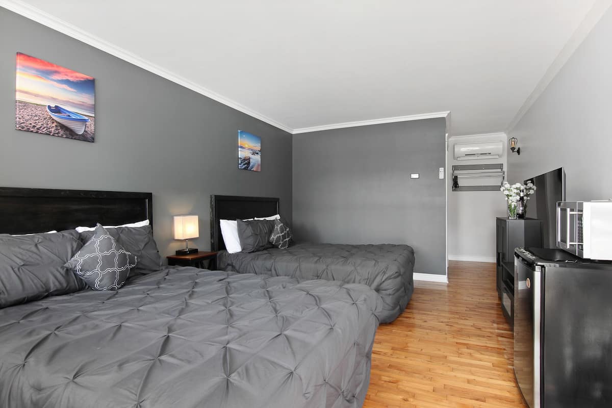 A modern bedroom with two beds, a wooden floor, a built-in TV, and an air conditioning unit.