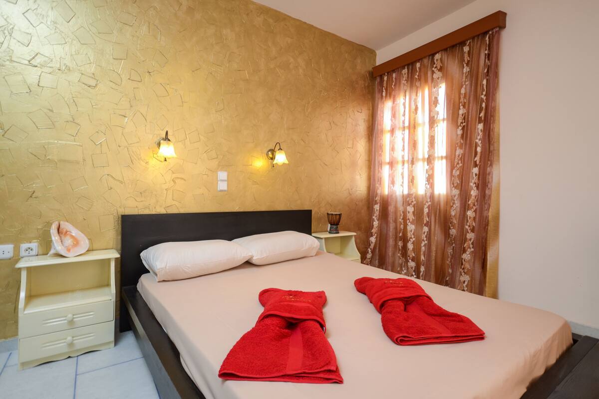 A hotel room with a bed, two bedside tables, a nightstand, a wall with a textured pattern, and a window with curtains.