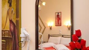 A hotel room with a bed, bedside table, a mirror, a painting, a vase with flowers, and a telephone. - Kahlua Studios (Naxos)
