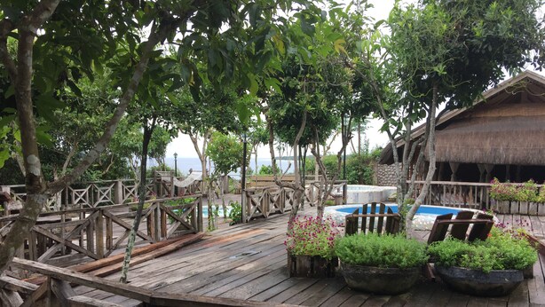 A wooden deck with a pool, surrounded by lush greenery and a thatched-roof structure. - Bohol Bee Farm (Dauis)