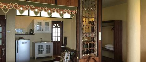 A room with a wooden cabinet, a small kitchenette, a decorative mirror, and a wooden chair.