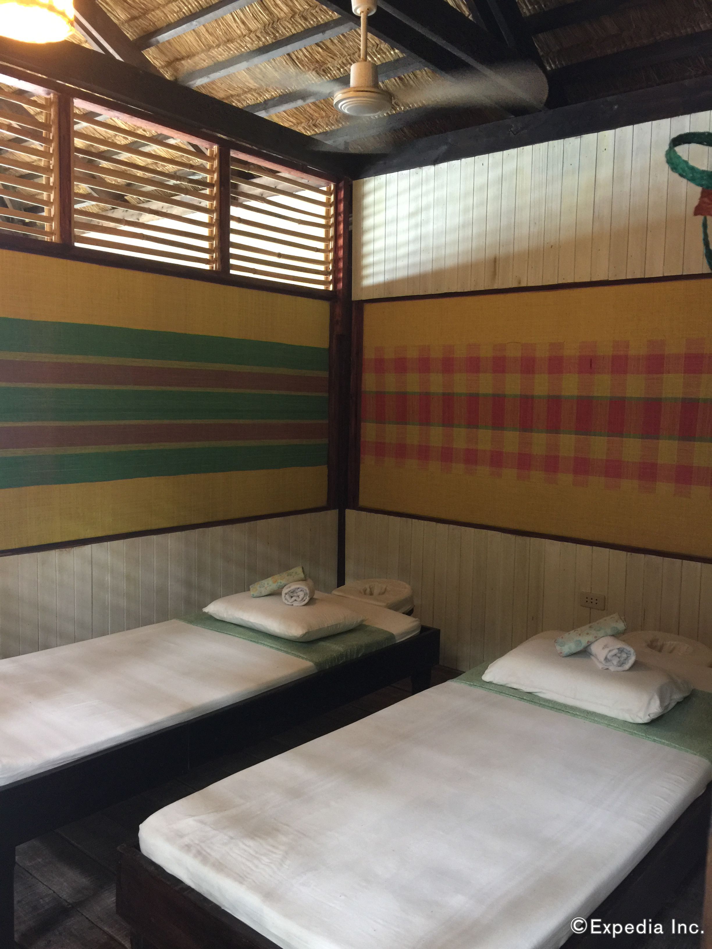 Quarto com duas camas, cabeceiras de madeira, teto de palha e janela com persianas.