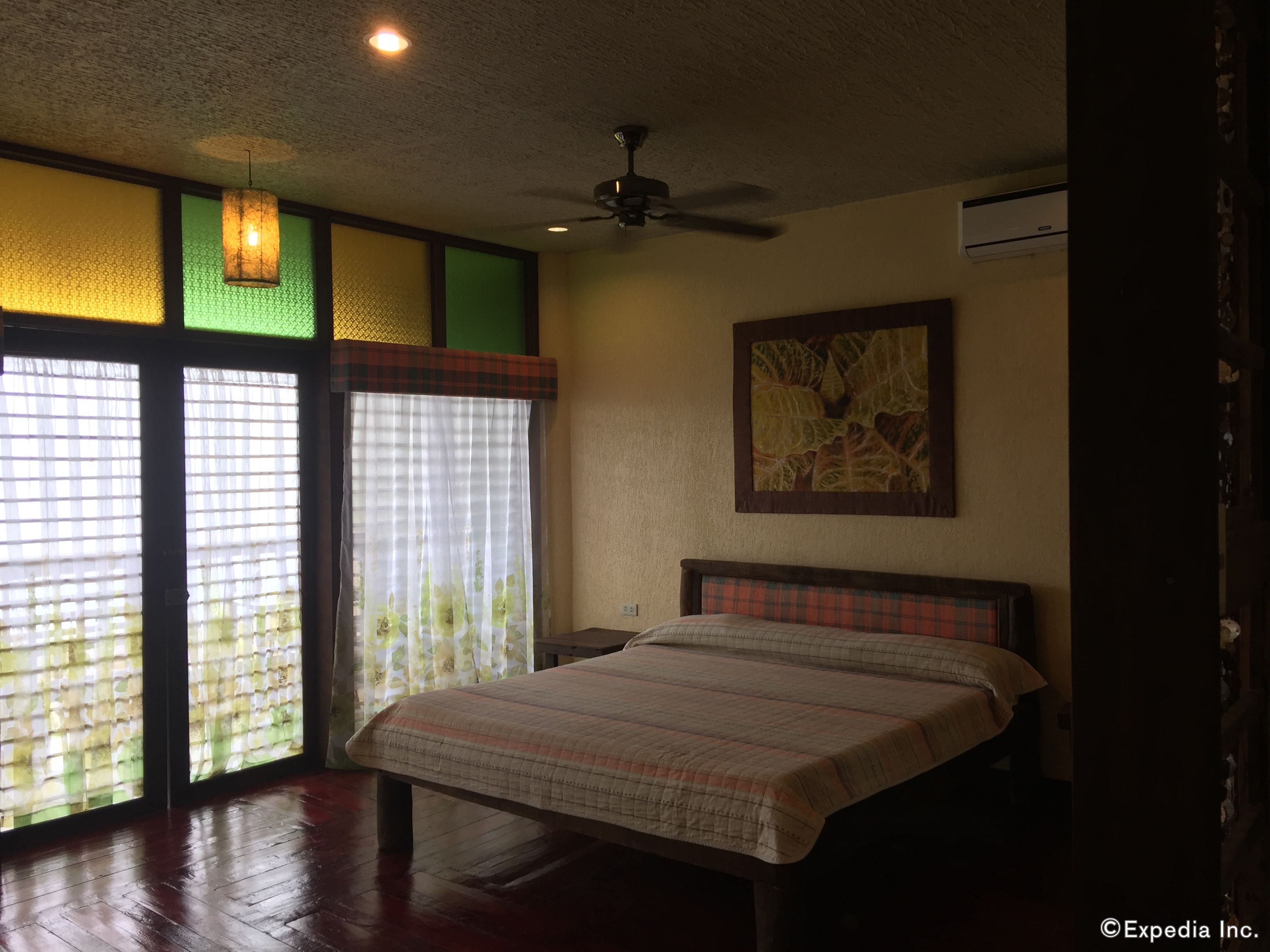 A bedroom with a bed, a ceiling fan, and a painting on the wall.