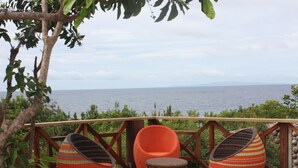A wooden deck with wicker chairs and a small table overlooking a body of water. - Bohol Bee Farm (Dauis)