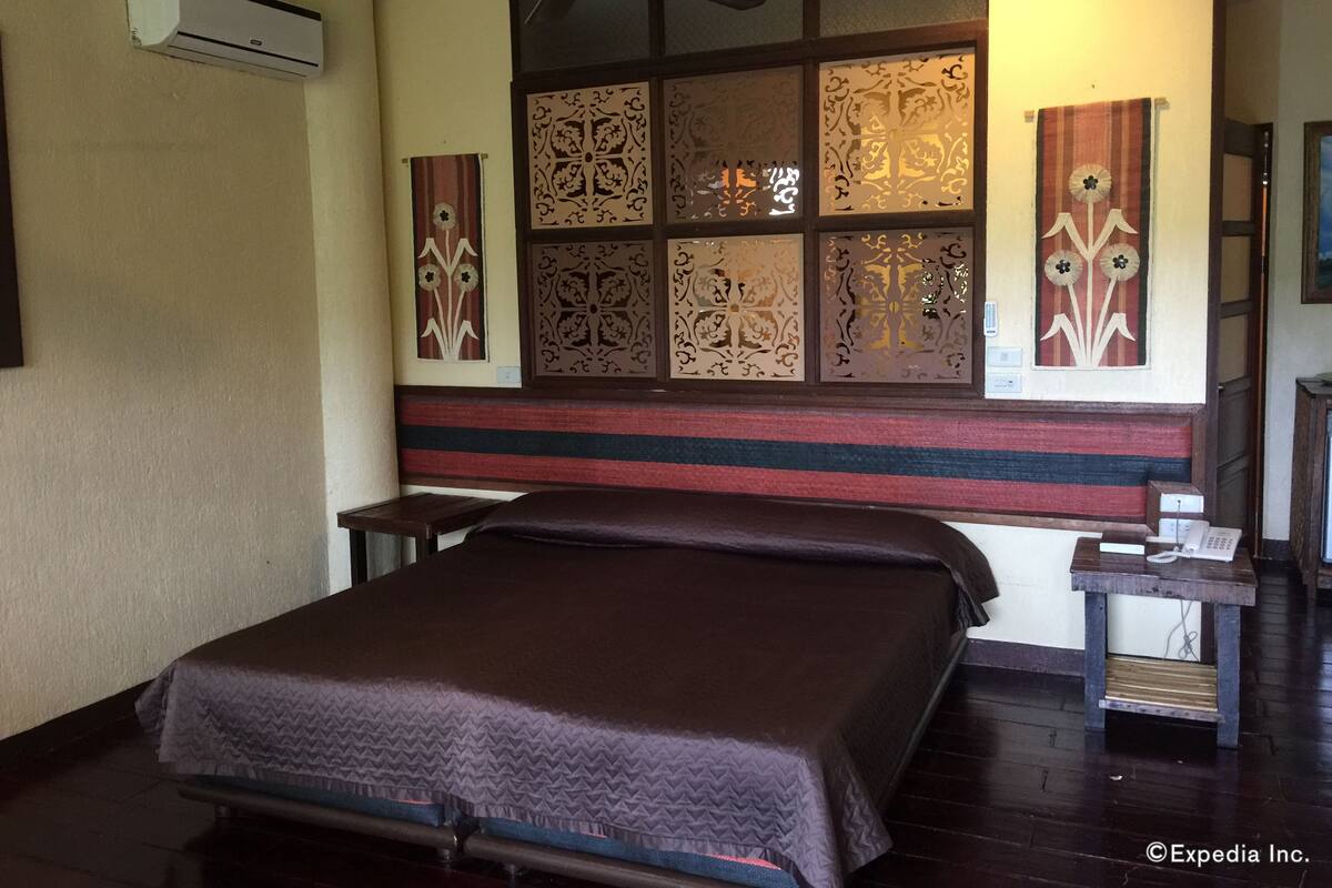 A hotel room with a bed, a ceiling fan, decorative panels, and a telephone on a wooden table.