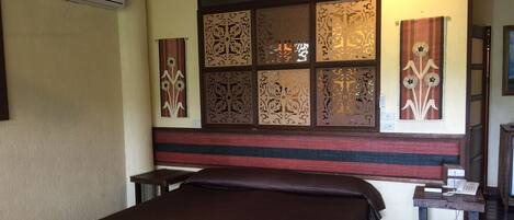 A hotel room with a bed, a ceiling fan, decorative panels, and a telephone on a wooden table.