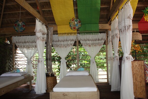 A room with two beds, each with white bedding and curtains. There are hanging decorations and a wooden ceiling.