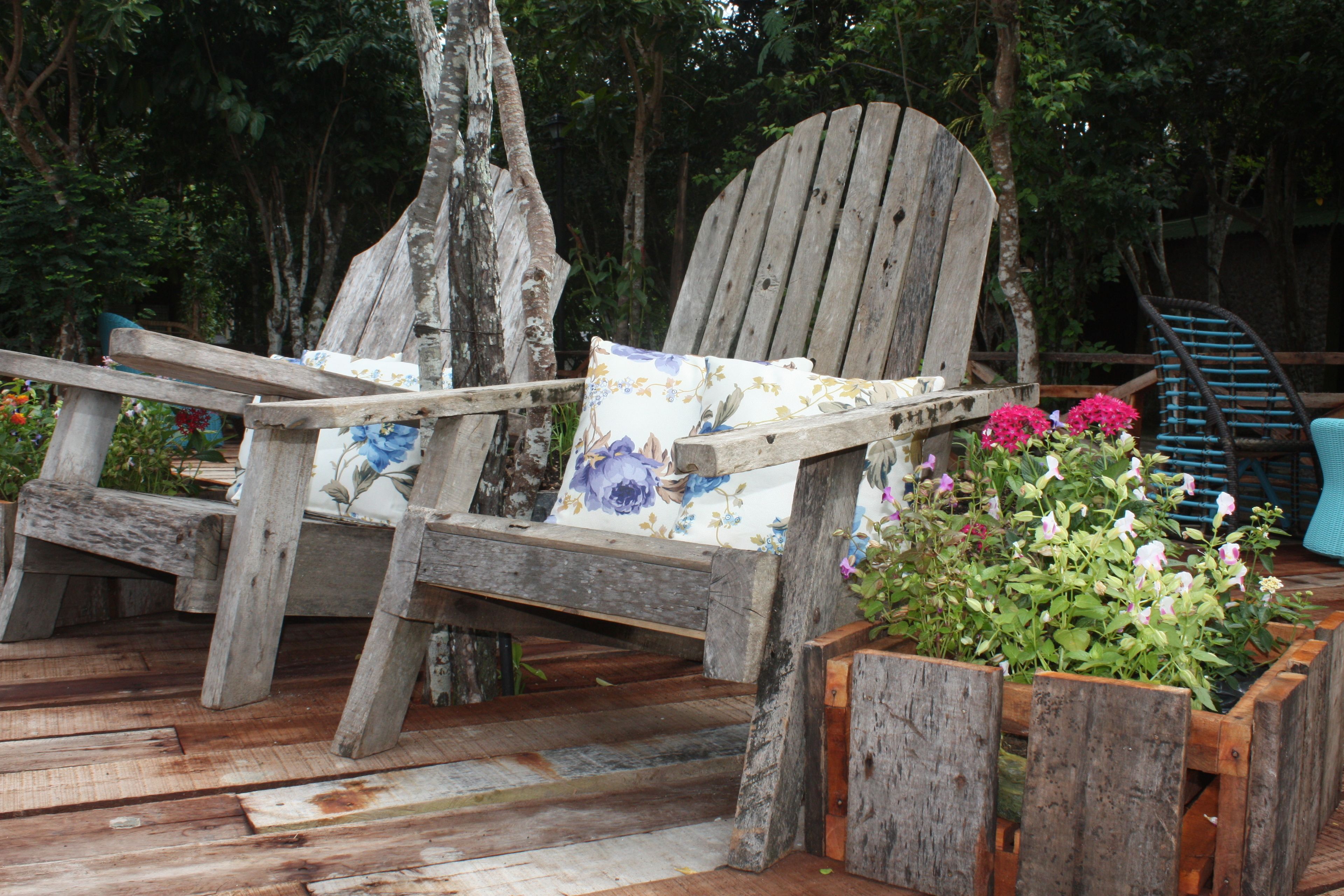 Una terraza rústica de madera con una silla de madera y una jardinera con flores.