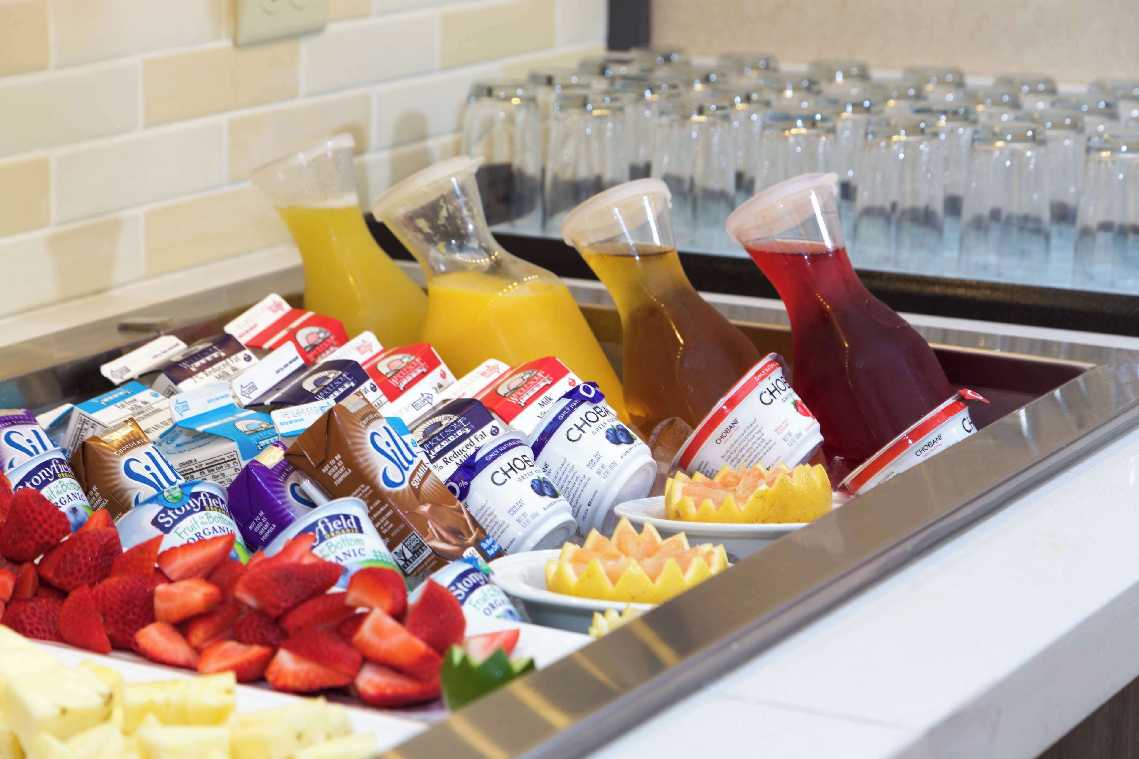 Un bufé con diversas opciones de comida y bebidas, entre ellas frutas, yogur y jugo.