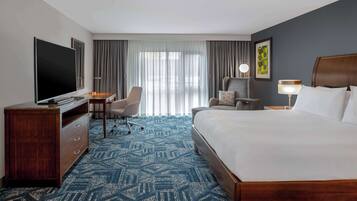 Une chambre d’hôtel avec un grand lit, un bureau avec une chaise, une télévision et une fenêtre avec des rideaux.