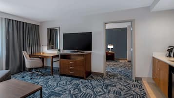 A hotel room with a desk, chair, television, and a large window with curtains.