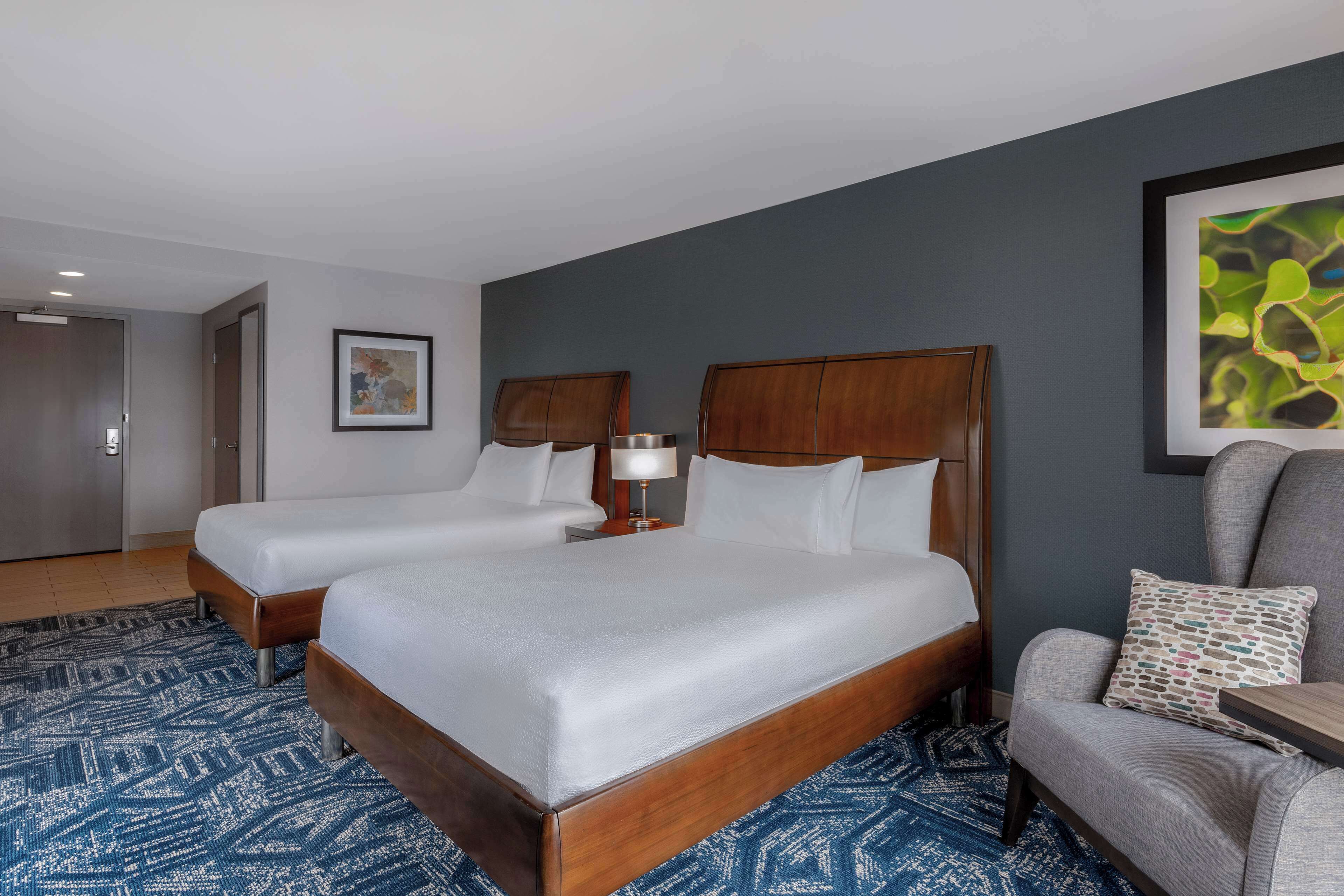 Une chambre d’hôtel avec deux lits, un bureau, une chaise et un grand tableau abstrait accroché au mur.