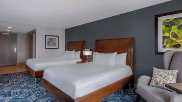 Une chambre d’hôtel avec deux lits, un bureau, une chaise et un grand tableau abstrait accroché au mur.