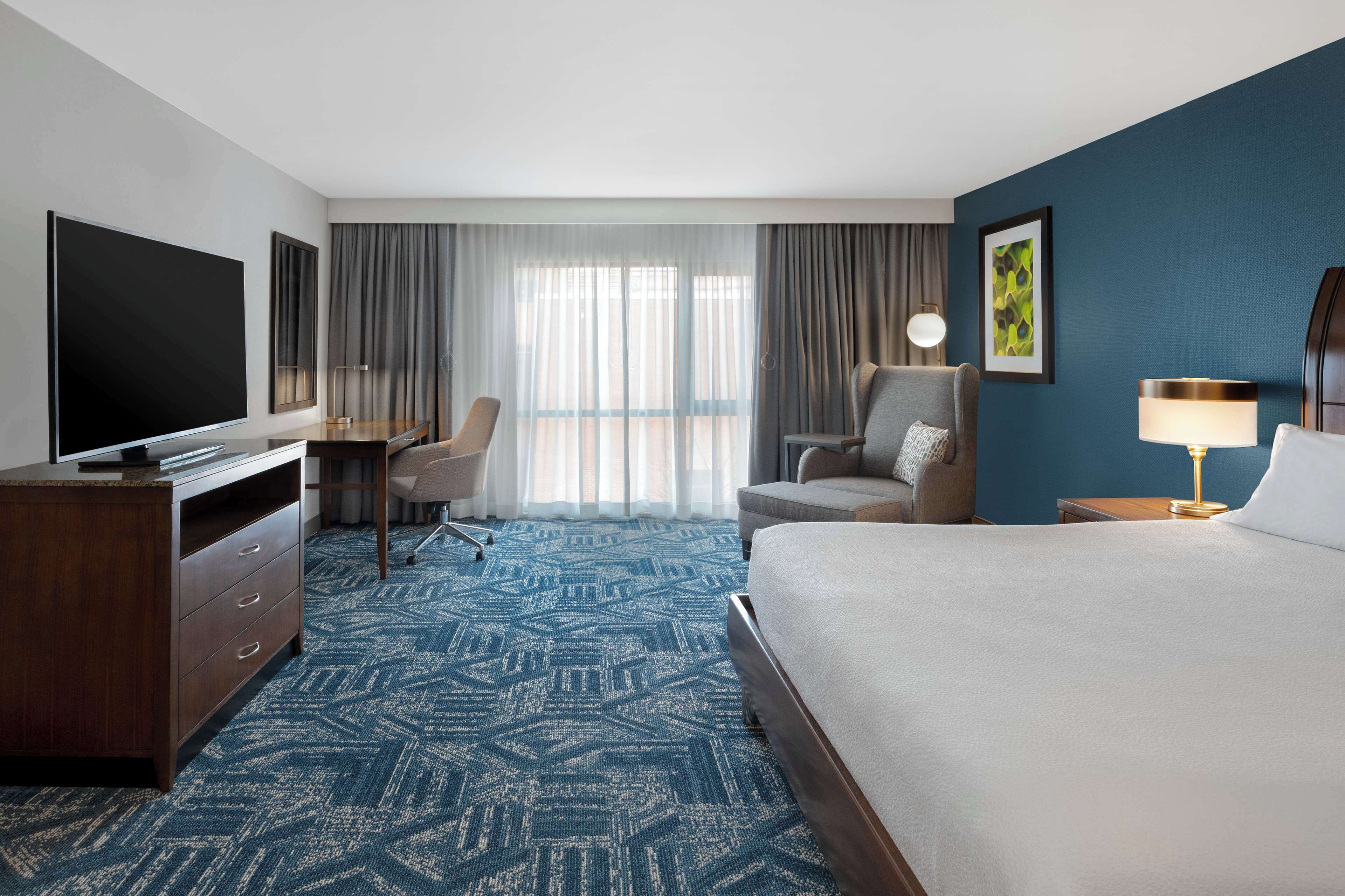 A hotel room with a large bed, a desk with a chair, a television, and a lamp.