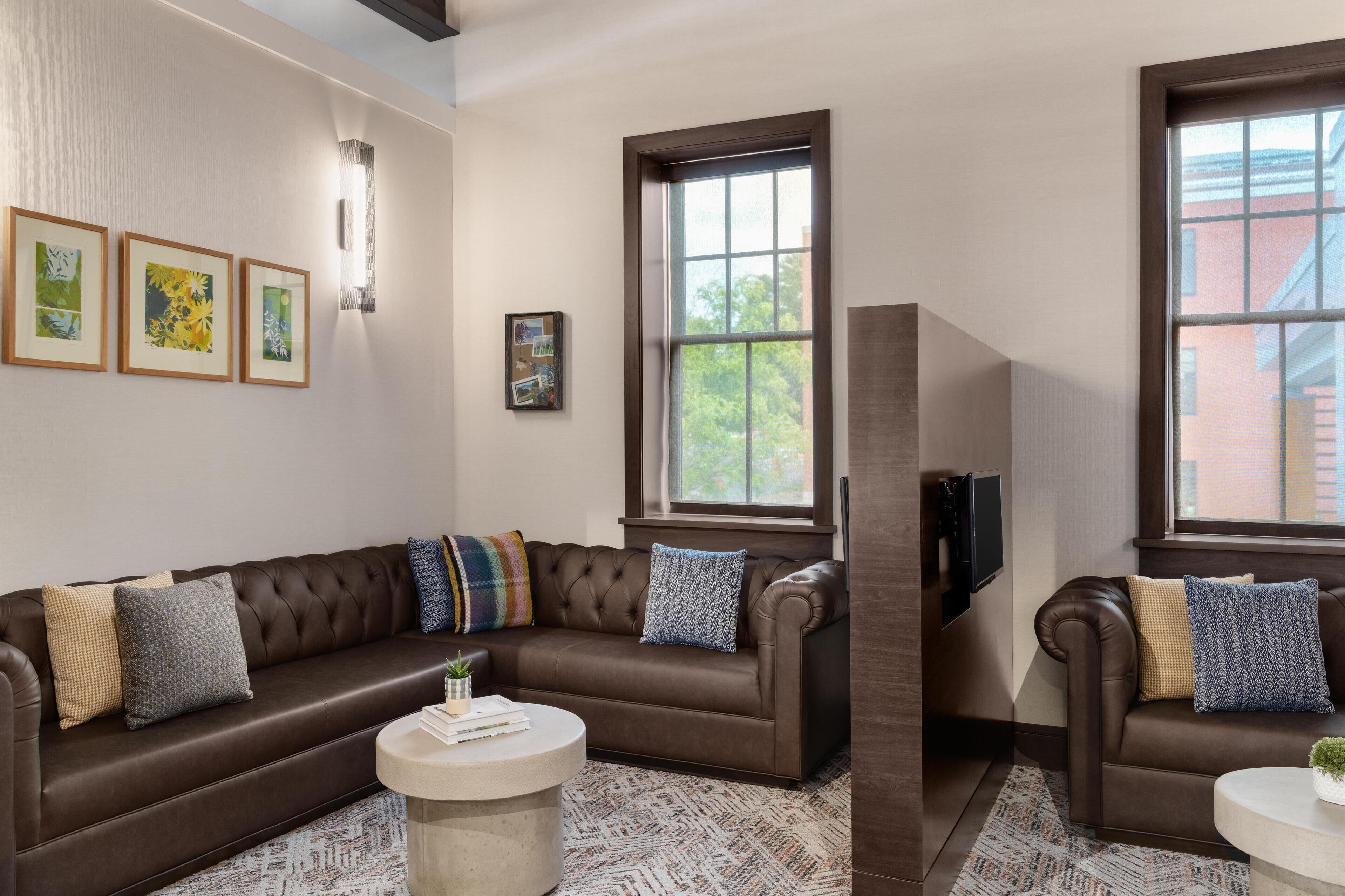 A modern living room with a brown leather sofa, two round coffee tables, and framed artwork on the wall.
