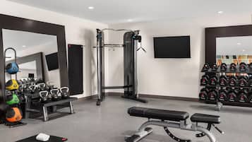 A modern gym with a squat rack, bench press, kettlebells, and a wall-mounted TV.
