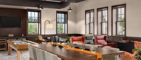 Una habitación amplia con una larga mesa de madera, asientos cómodos, una zona de bar y grandes ventanales que dejan entrar luz natural.