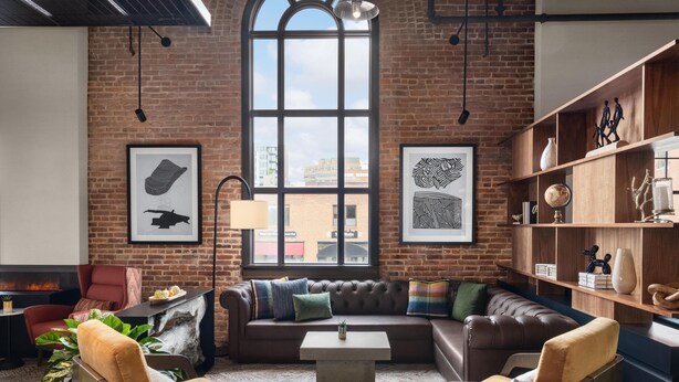 A cozy living room with a leather sofa, armchairs, a coffee table, and a fireplace. There are framed artworks on the walls and a bookshelf with decorative items.