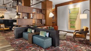 A modern lounge area with a sectional sofa, wooden shelving, and a patterned carpet.
