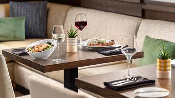 A dining area with a wooden table set for two, a bowl of salad, a plate of food, and glasses of wine.