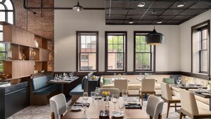 A modern dining area with a high ceiling, exposed brick walls, and large windows.