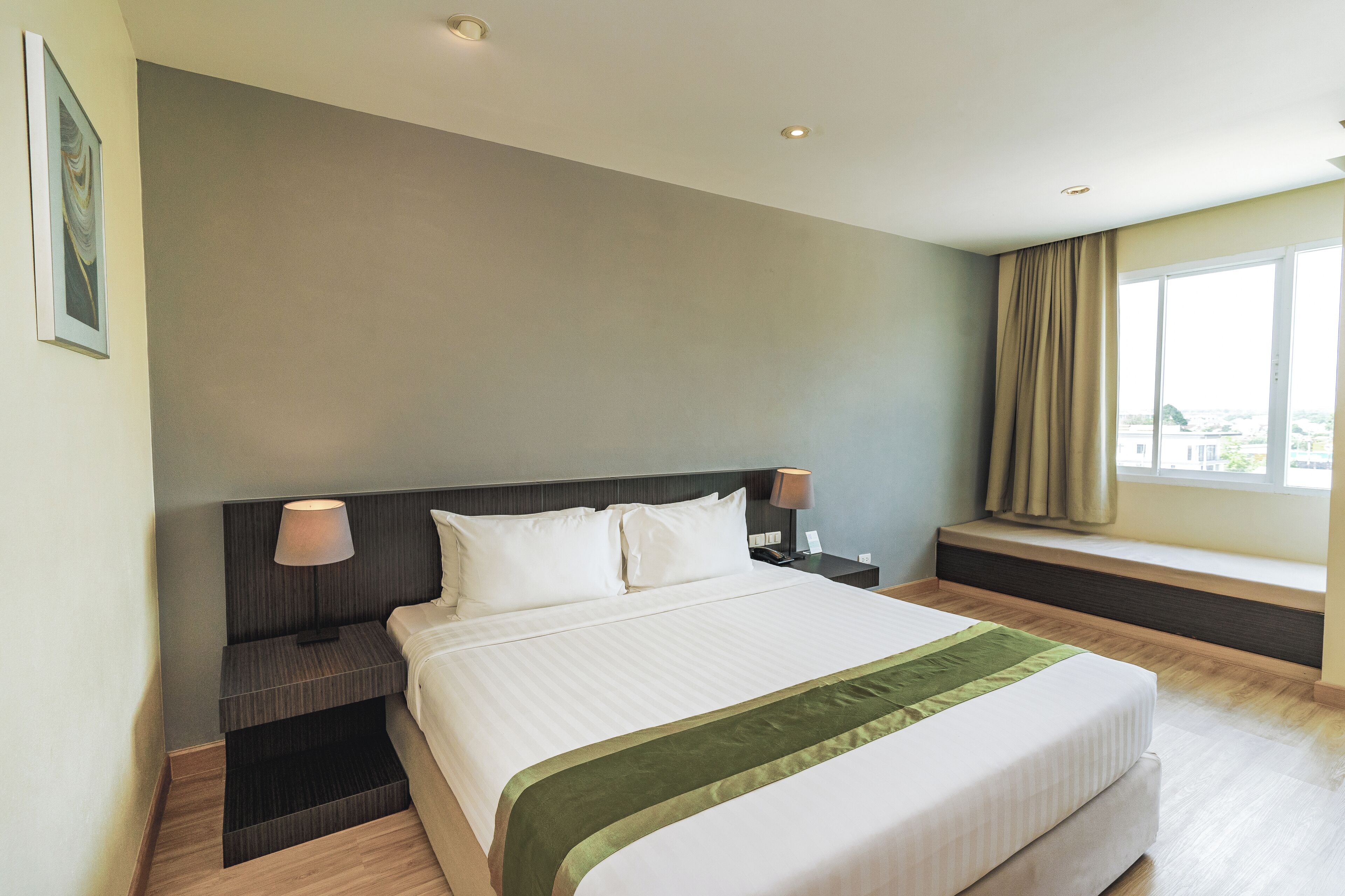 A hotel room with a large bed, bedside lamps, a window with curtains, and a view of the city.