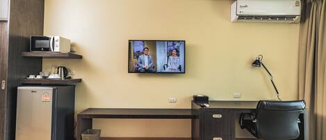 Habitación de hotel con kitchenette, televisor de pantalla plana, escritorio con silla y aire acondicionado.