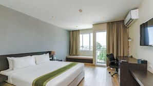 A hotel room with a large bed, a desk, a chair, a TV, and a window with curtains. - Tamarind Garden Hotel (Rayong)