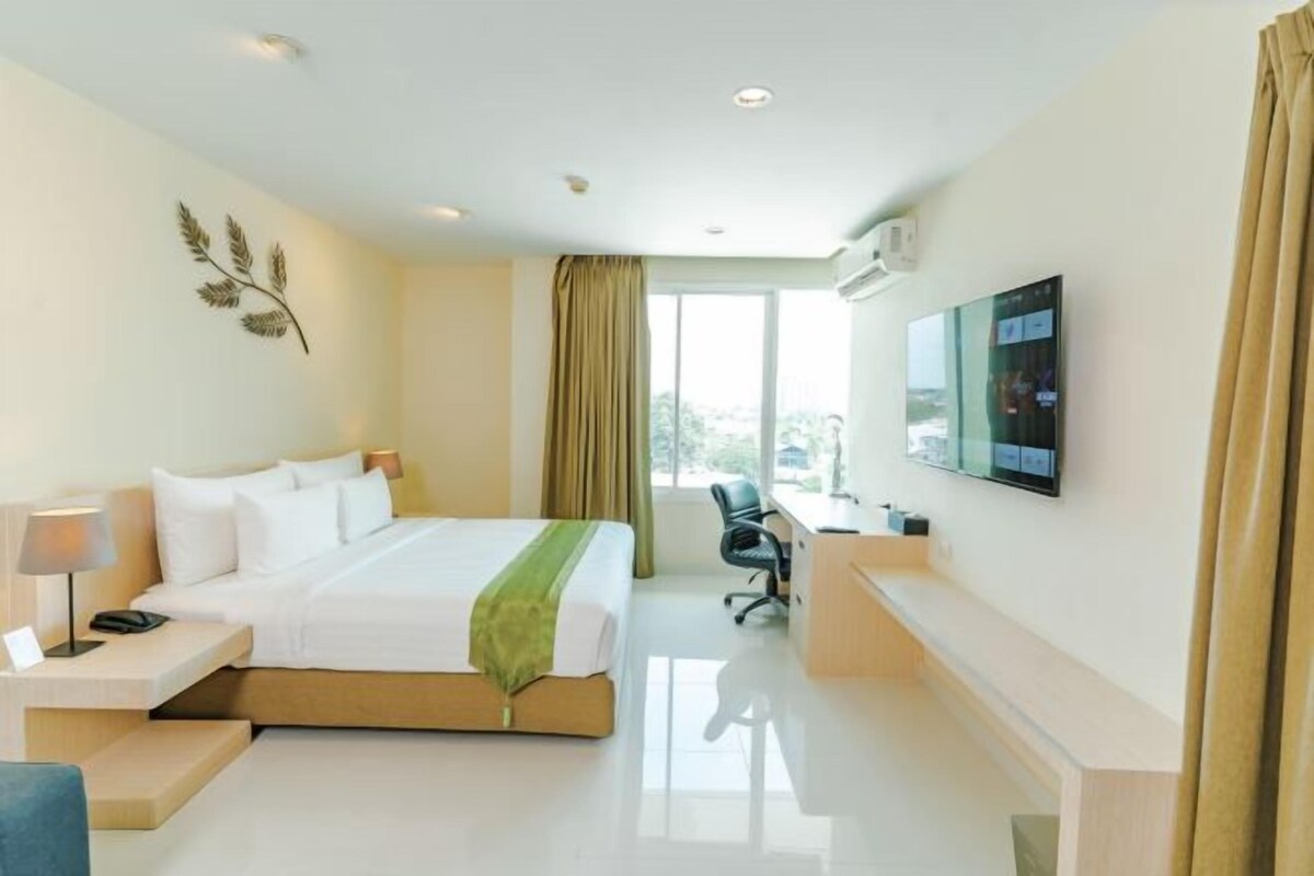 A hotel room with a bed, a desk, a chair, a TV, and a window with curtains.