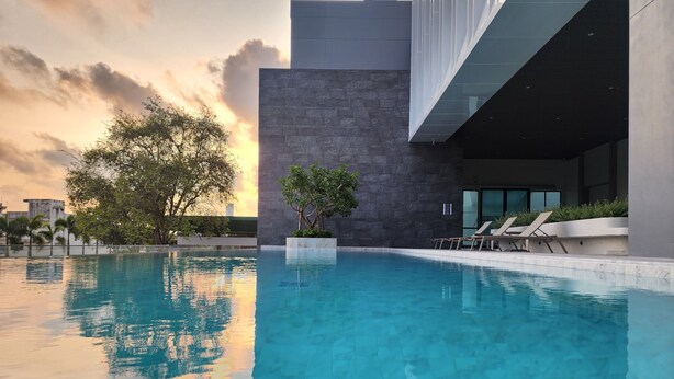 A modern pool area with clear blue water, a stone wall, and lounge chairs. - Tamarind Garden Hotel (Rayong)