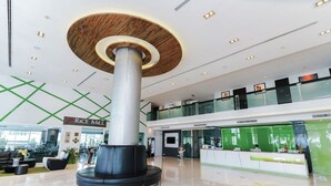 A modern hotel lobby with a central column, a reception desk, and a dining area. - Tamarind Garden Hotel (Rayong)