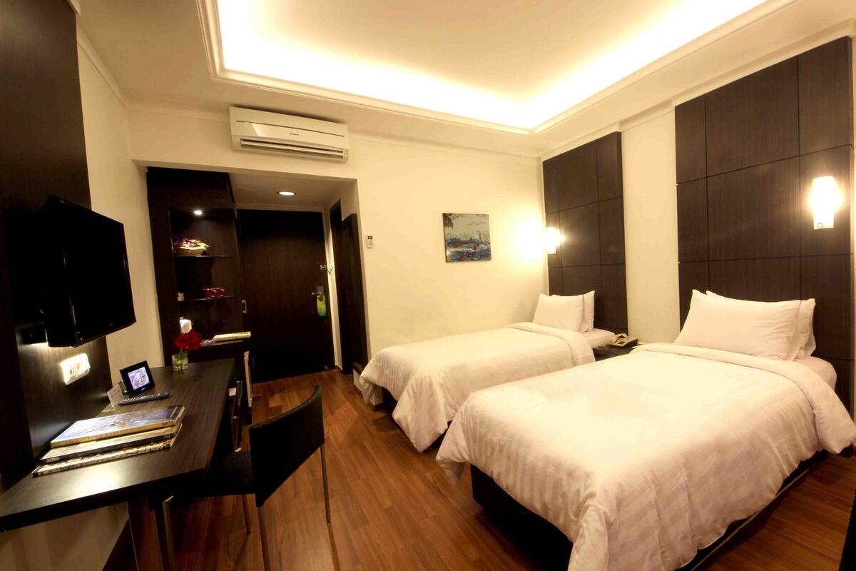A hotel room with two beds, a desk with a computer, a TV, and a painting on the wall.