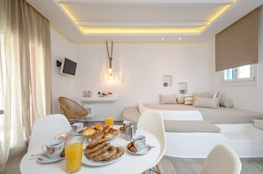 A modern hotel room with a breakfast setup including croissants, eggs, and orange juice. - Depis Edem Luxury Villas (Naxos)