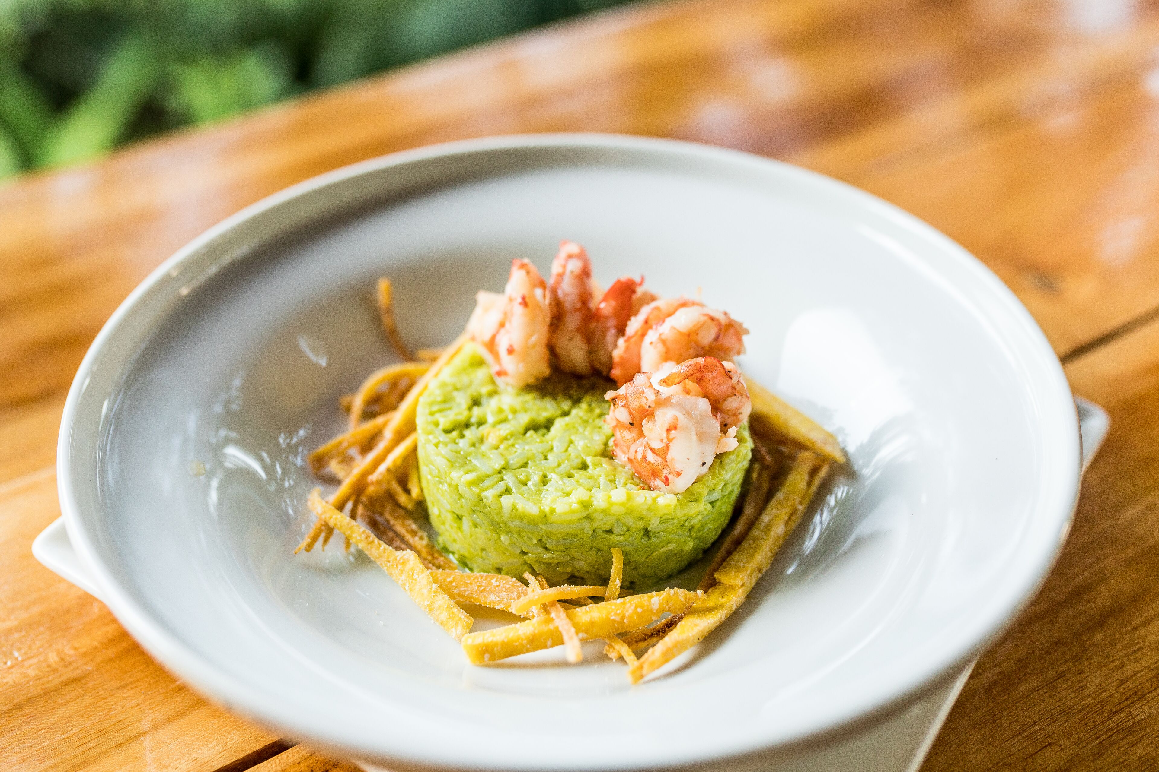 A plate with a green avocado-based dish, shrimp, and crispy strips on a wooden table.