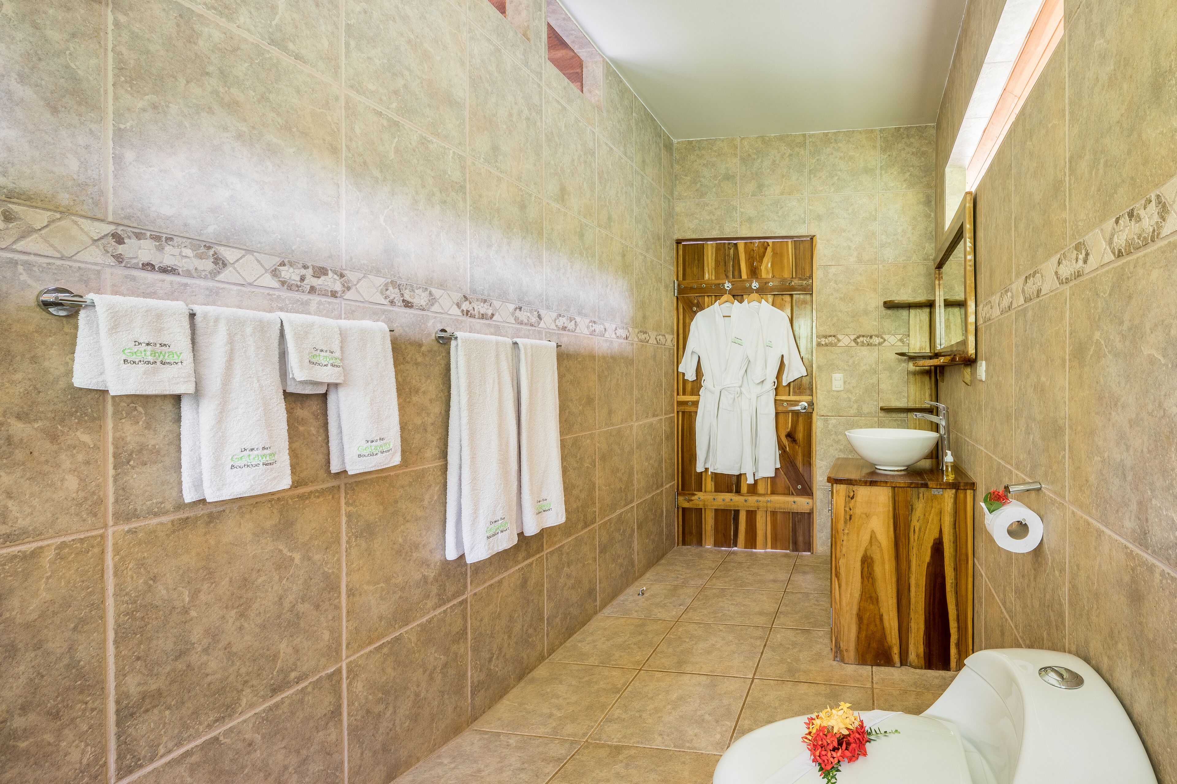 A bathroom with a wooden vanity, a sink, and a toilet. There are towels hanging on the wall and a mirror above the sink.